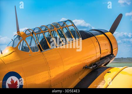 Side view close-up of vintage yellow military training aircraft cockpit and fuselage on runway. Multiple canopy frames visible along tandem seating co Stock Photo