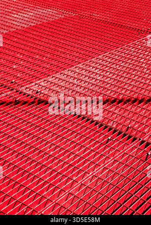 Red metal grid, diagonal pattern. Interlaced bars create a geometric texture. Suitable for architecture, industry, or abstract design concepts. Stock Photo