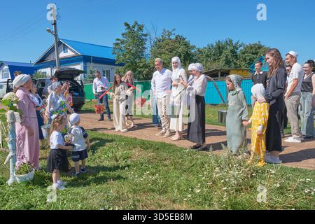 Ufa, Russia: August 2, 2025: Lively scene from traditional Tatar village wedding. Bride and groom, Guests, in festive attire gather outdoors on bright Stock Photo
