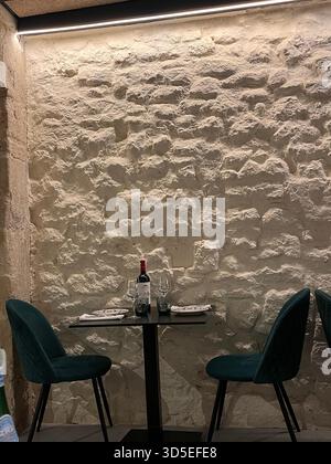 Intimate dining corner with a small table set for two against a textured white stone wall in Alicante, Spain. Includes wine, glasses, Stock Photo