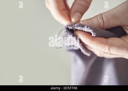 Close-up of person's hands mending purple fabric with needle and thread focus on precision and care Stock Photo