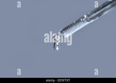 Close-up of transparent liquid drop from glass pipette against light blue background Stock Photo
