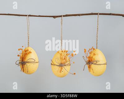 Three Easter eggs with dried flowers for decoration hanging on a branch on a gray background Stock Photo