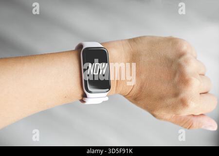 Close-up of a person s wrist wearing a modern smartwatch with the word now displayed on the screen, motivational and minimalist style, concept of time Stock Photo