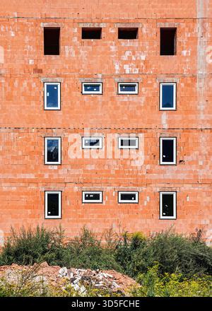 New apartments block construction site, wall made of orange bricks with some windows already installed Stock Photo
