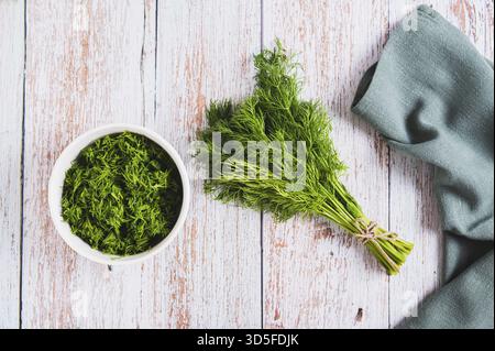 Bunch of fresh dill and chopped dill in a bowl on a table top view Stock Photo