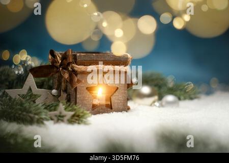 Christmas lantern with warm glow, fir branches, ornaments and hanging festive lights on snow and blue background Stock Photo
