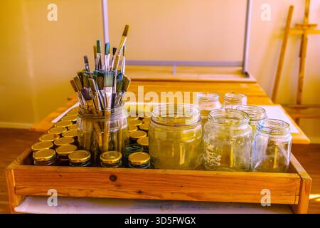 potbelly pig. Art supplies are neatly arranged in a wooden tray, featuring jars and brushes, creating an inviting workspace for creativity Stock Photo