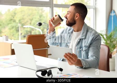 Young man drinking coffee and using tablet for online work at home Stock Photo