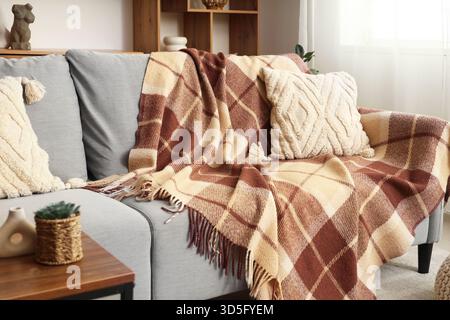 Soft checkered blanket on sofa, pouf and coffee table in interior of modern room Stock Photo