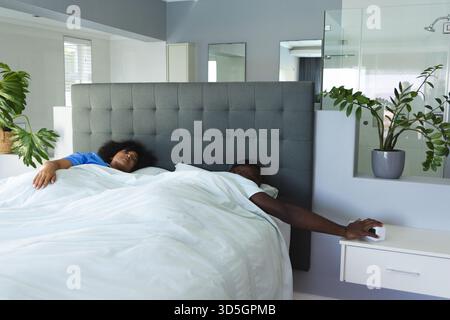 African American couple relaxing in bed, reaching for alarm clock in modern bedroom Stock Photo