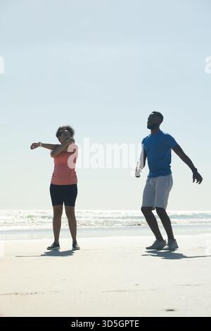 African American couple exercising on beach, stretching and jogging together Stock Photo