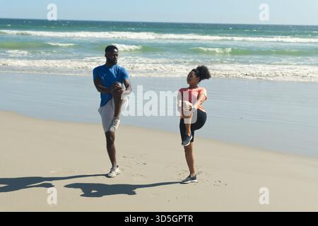 African American couple exercising on beach, stretching legs and enjoying sunny day Stock Photo