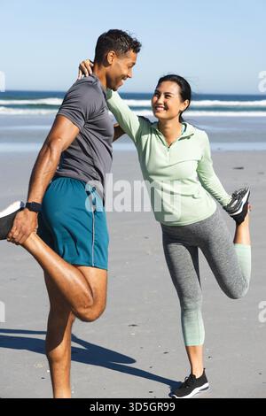Couple stretching on beach, smiling and enjoying morning exercise together Stock Photo