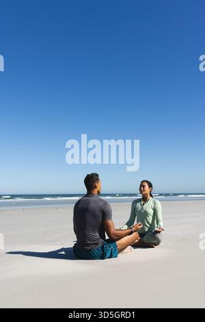 Couple meditating on beach, enjoying peaceful moment under clear blue sky, copy space Stock Photo