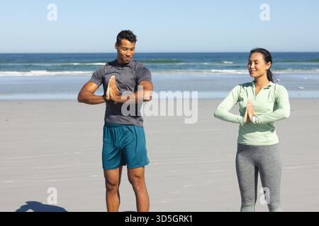 Couple practicing yoga on beach, enjoying peaceful morning by ocean Stock Photo