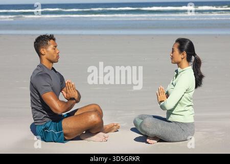 Meditating on beach, couple sitting cross-legged, focusing on mindfulness and relaxation Stock Photo