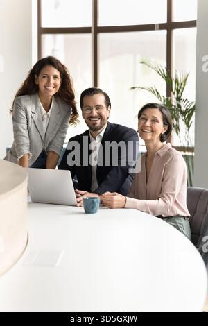 Three smiling diverse business colleagues using notebook looking at camera Stock Photo