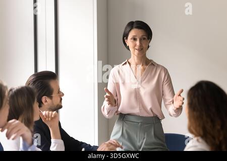 Smiling mature businesswoman speaking to diverse staff at corporate meeting Stock Photo