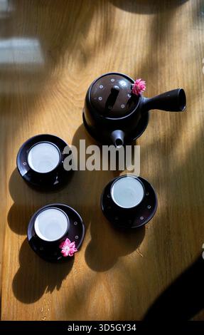 Flat lay photo of ceramic tea pot and three tea cups on wood table under sunlight Stock Photo