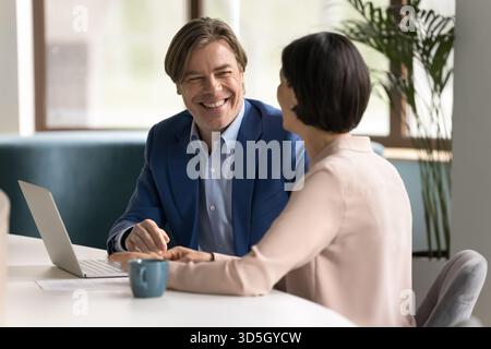 Two happy professionals collaborate on project using laptop at workplace Stock Photo