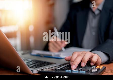 Business man calculating a financial report using a calculator and laptop. Professional accounting and tax paperwork, corporate finance and investment Stock Photo