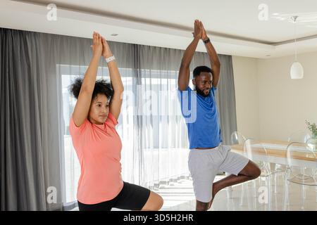 Couple practicing yoga together at home, balancing in tree pose with focus Stock Photo