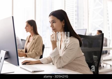 Focused pensive young business professional woman working at pc monitor Stock Photo