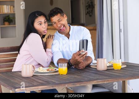 Couple making funny faces taking selfie during breakfast on patio table Stock Photo