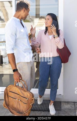 Couple discussing plans while woman talks on smartphone, holding man's arm Stock Photo