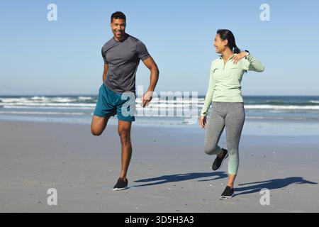 Couple exercising on beach, stretching legs and smiling in morning sunlight Stock Photo