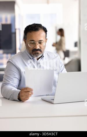 Focused busy senior Indian businessman analyzing financial document Stock Photo