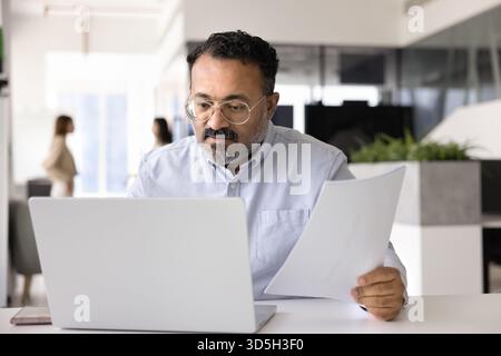 Busy serious senior Indian professional man working on financial reports Stock Photo