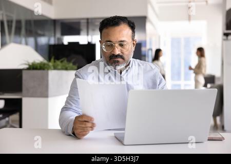 Serious elder mature Indian business leader man reading legal document Stock Photo