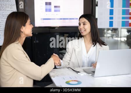 Happy young diverse female coworkers shaking hands Stock Photo