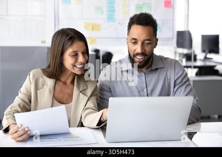 Two happy young multiethnic colleagues working together at laptop Stock Photo