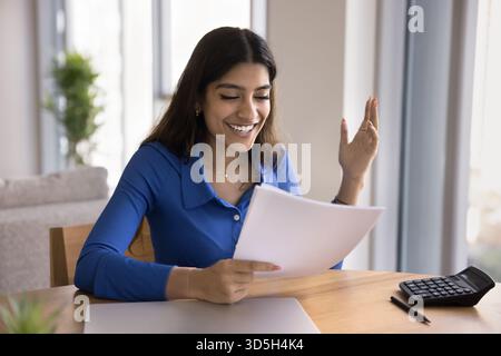 Cheerful excited young Indian freelancer woman reading legal document Stock Photo