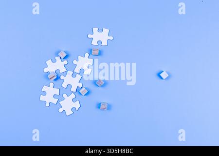 Scattered puzzle pieces and wooden cubes on blue surface suggest individuality, separation, and the interplay between structure and randomness. Stock Photo