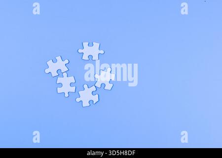 Scattered puzzle pieces and wooden cubes on blue surface suggest individuality, separation, and the interplay between structure and randomness. Stock Photo