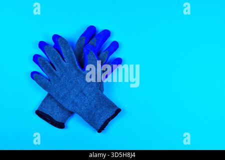 Gray work gloves with blue rubber coating on bright blue background represent personal protective equipment for grip, safety, and manual labor. Stock Photo