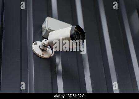 Exterior surveillance camera on ribbed metal cladding using adjustable bracket, providing focused monitoring, durable housing design and stable securi Stock Photo