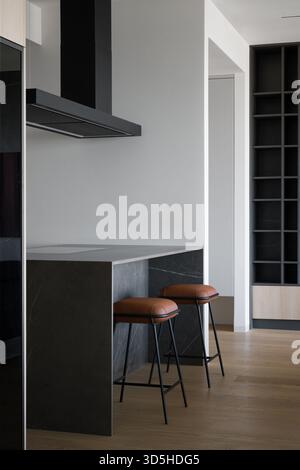 Interior of a modern and stylish kitchen featuring a dark marble island with a breakfast bar. Two elegant bar stools with brown leather seats and blac Stock Photo