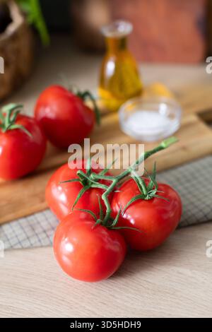 Fresh red vine tomatoes arranged on a wooden cutting board and a checkered cloth napkin. A small bottle of olive oil and a glass bowl of sea salt are Stock Photo