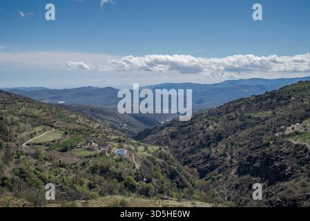 The Palancon ravine in Bayarcal, Almería, Spain, features rugged cliffs, terraced slopes, and lush greenery under a bright blue sky with drifting clou Stock Photo