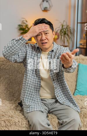 Face palm. Shame on you. Upset man making disrespect gesture, feeling bored disappointed in fail results bad news. Portrait of Middle Eastern guy in home living room sitting on couch sofa. Lifestyles. Stock Photo