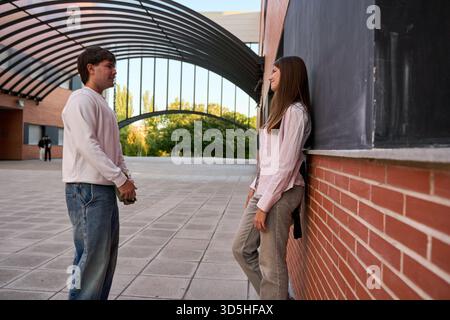 Young students standing, talking and smiling at each other on a university campus, representing education, friendship, and communication Stock Photo