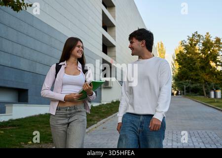 Two young students walking and talking on a modern university campus, sharing a laugh and enjoying student life Stock Photo