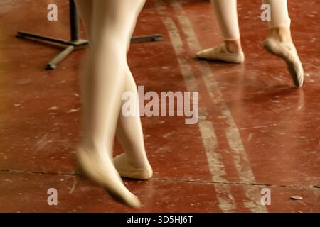 Ballet dancers focus on their technique while practicing in a wooden-floored studio during a training session. Stock Photo