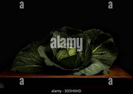 Fresh green cabbage displayed on a wooden table against a dark background in a dramatic still-life composition. Stock Photo