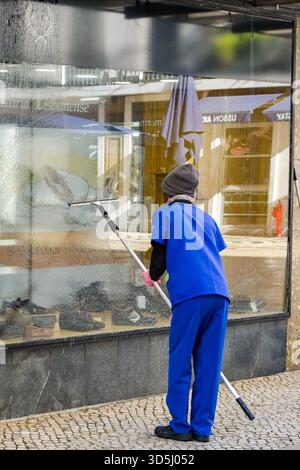 Lisbon, Portugal - 13 January 2025: Person cleaning the window of a shop in the city centre Stock Photo